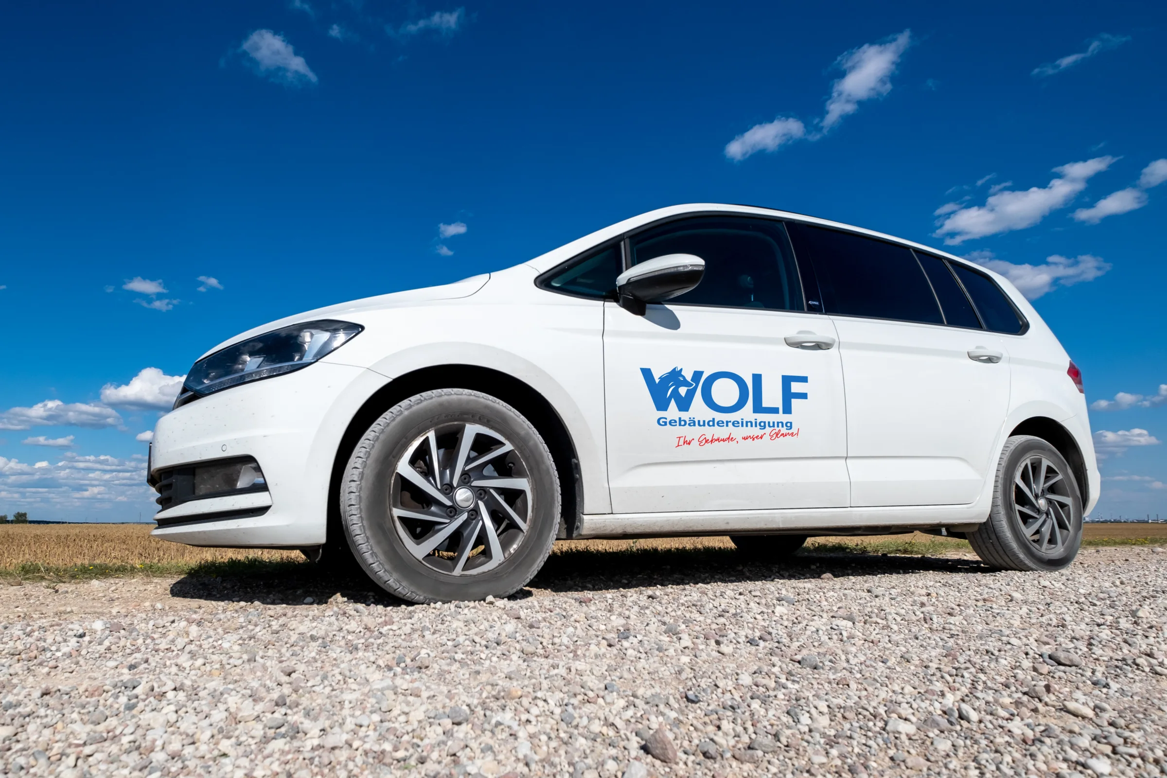 Weißer VW Touran der Wolf Gebäudereinigung mit Logo auf der Fahrertür, vor blauem Himmel