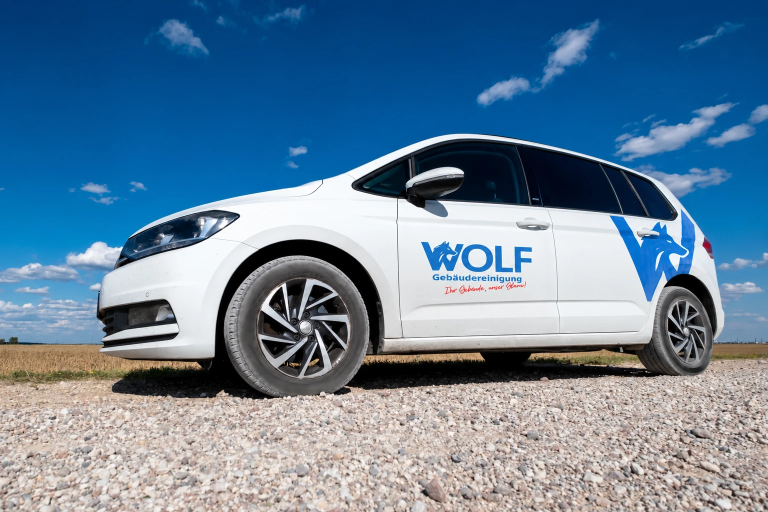 Weißer VW Touran der Wolf Gebäudereinigung mit Logo auf der Fahrertür, vor blauem Himmel